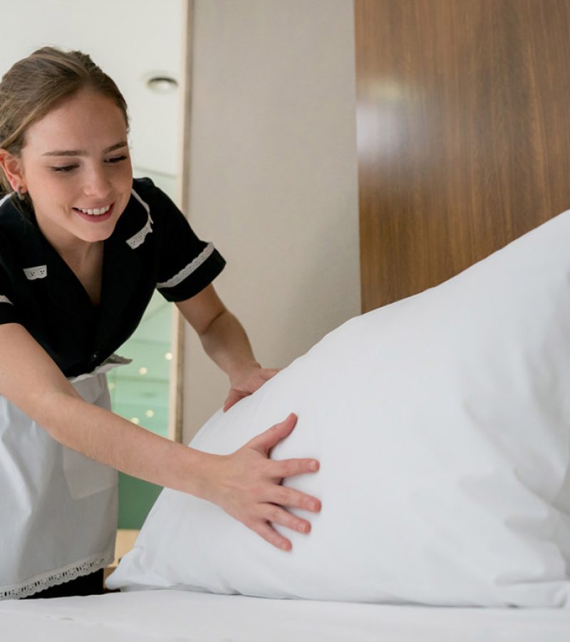 Beautiful housekeeper making the bed at a hotel looking happy and smiling